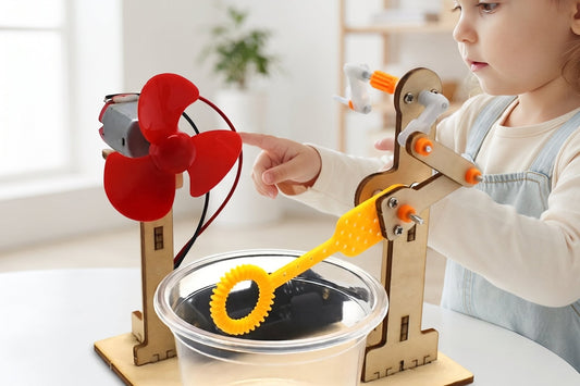A young child points at the red fan on a wooden bubble machine kit set up on a table.